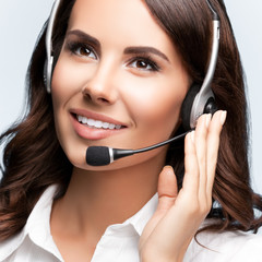 Portrait of cheerful support female phone operator in headset, against grey