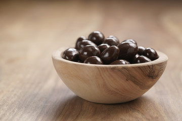 chocolate covered almonds in wood bowl on table, with copy space