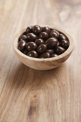 chocolate covered almonds in wood bowl on table, with copy space