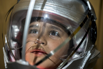Childhood, Boy playing to be an astronaut with a space helmet and silver suit on metallic background