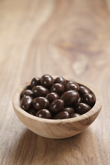 chocolate covered almonds in wood bowl on table, with copy space