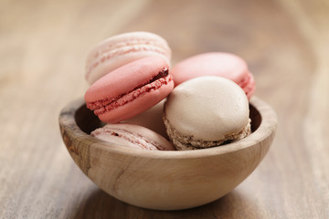pastel colored macarons with strawberry, rose and caramel flavour in wood bowl on table