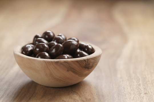 chocolate covered almonds in wood bowl on table, with copy space