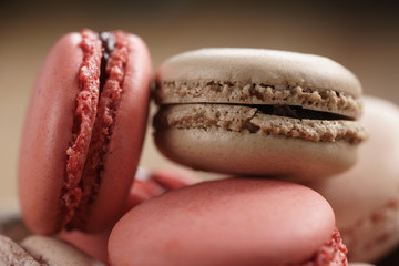 closeup shot of pastel colored macarons with strawberry, rose and caramel flavour in wood bowl, macro photo
