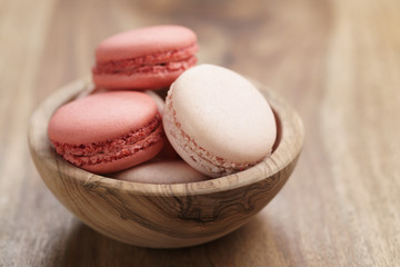 pastel colored macarons with strawberry and rose flavour in wood bowl on table