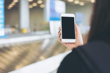 A woman holding and using mobile phone while waiting for baggage claim in the airport 