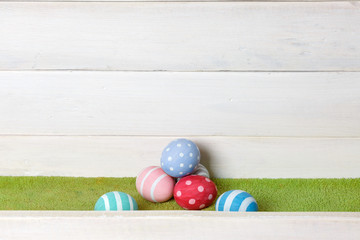 Several colorful easter eggs handmade lie on a pile on a green lawn against a wooden surface background