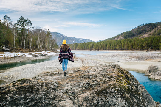 woman in blue jeans and Hiking bag stands on the shore of a mountain lake and looking into the distance