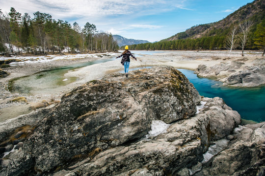 woman in blue jeans and Hiking bag stands on the shore of a mountain lake and looking into the distance