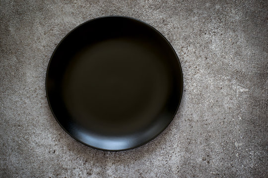 Empty black ceramic plate On a concrete background. Top view with copy space