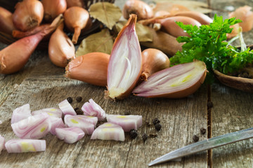 Whole and chopped shallot onion on a wooden background with green parsley leaves and a bay leaf. Shallow depth of field.