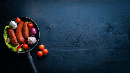 Grilled sausages in a pan with fresh vegetables. Wooden surface. Top view.