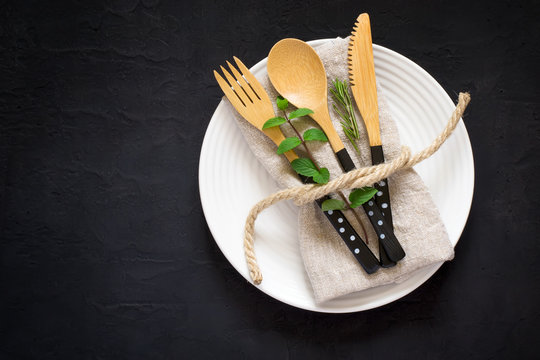 Natural table setting with bamboo knife fork and spoon on a black background, Top view with copy space