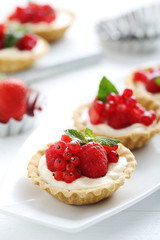 Dessert tartlets with berries on white wooden background