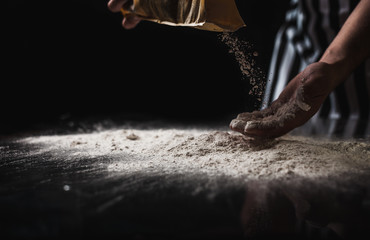 A man cooks in an apron cooking from a flour on a glass table with a reflection