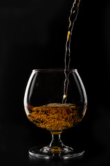 brandy or whiskey pouring into glass on a black background