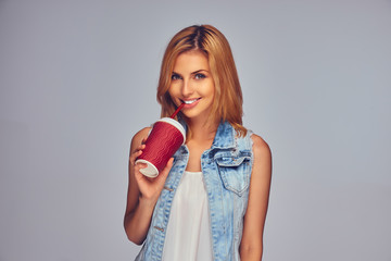 Positive and the smiling blond female holds paper red cup with juice.