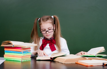 Young girl reading a book near empty green chalkboard