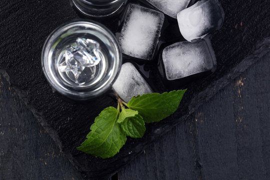 Vodka in shot glasses and ice on rustic wood background