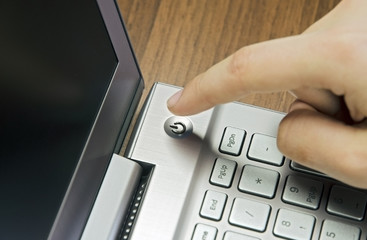 Closeup view of a hand with a finger, press the power button on metallic silver laptop keyboard,...