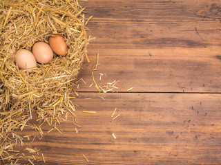Brown eggs in hay nest. Rural eco background with brown chicken eggs and straw on the background of old wooden planks. Top view. Creative background for Easter cards, restaurant menu or design