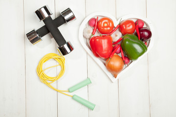 Fototapeta na wymiar Sport and diet. Healthy lifestyle. Vegetables, dumbbells. Peppers, tomatoes, garlic, onion radish in a heart on white background