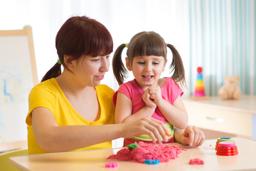 Cute child girl and mother playing with kinetic sand at home