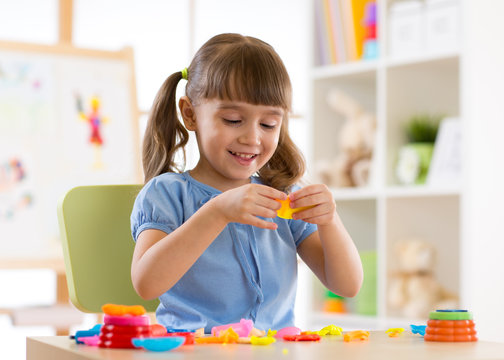 Little kid girl is playing with plasticine while sitting at table