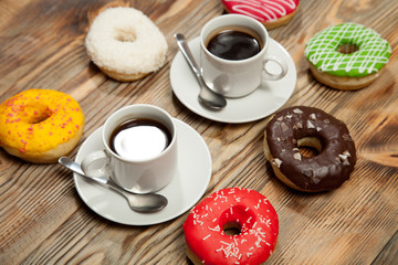 Two cups with coffee and donuts on a wooden background