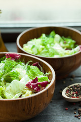 A dish of fresh salad frisse, Romano and radiccio with olive oil, salt and freshly ground percec in a wooden bowl