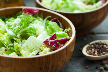 A dish of fresh salad frisse, Romano and radiccio with olive oil, salt and freshly ground percec in a wooden bowl