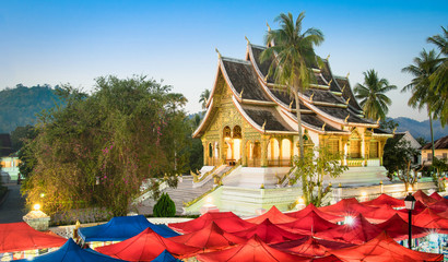 Wat Xieng Thong temple and night market at blue hour in Luang Prabang - Laos PDR world famous tourism destination - Travel concept with antique landmark in south east Asia exclusive city destinations