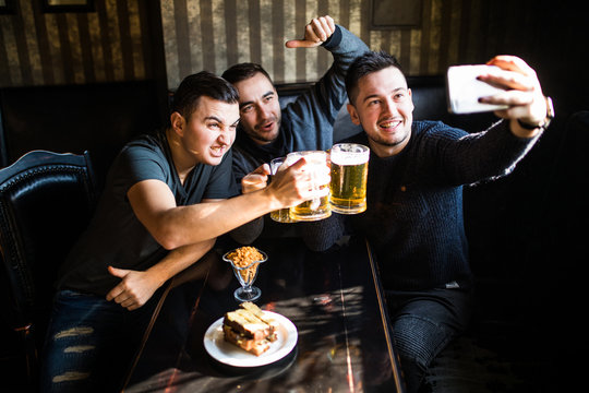 happy male friends taking selfie and drinking beer at bar or pub on party