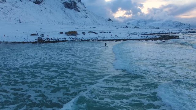 Surfers are training on Scagsanden beach in Lofoten islands in winter evening time, view from above