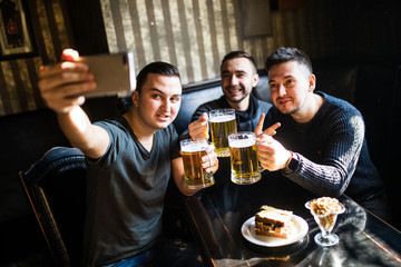 Handsome friends having fun taking selfie and drinking draft beer in pub.