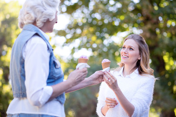 Amused young woman enjoying ice cream with aged mother outdoors