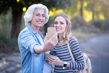 Smart retired woman testing gadget with pregnant daughter outdoors