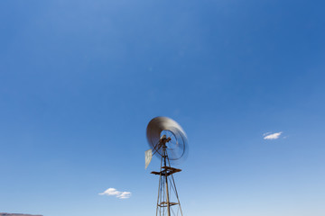 Close up wide angle image of a windmill / windpomp with spinning blades, pumping water in the Tankwa Karoo in South Africa on a hot summersday