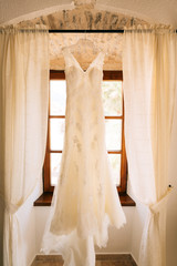 The bride's dress hangs on the cornice on the window.