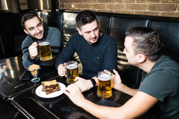 Meeting with the best friends. Three happy young men in casual wear talking and drinking beer while sitting in bar together