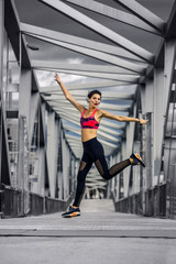 Portrait of young and sporty woman in sportswear jumping on the bridge in Port Forum, Barcelona, Spain.