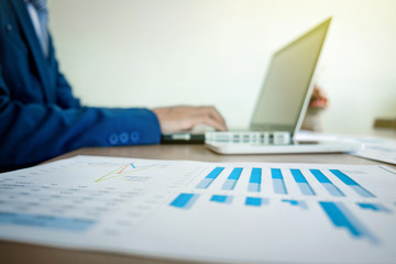 Image of business, Business man working at office with laptop and graph data documents on his desk, blurred background.