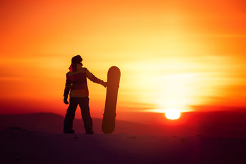 Woman snowboarder silhouette on sunset backdrop