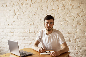 Concentrated writer working on writing new chapter of article sitting in modern home loft interior and look to the camera.Smart male journalist use laptop to find information via internet