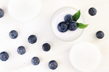 Blueberry facial cream in jar with fresh berries scattered white wooden background, top view. 