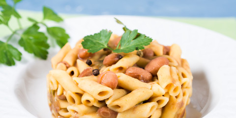 Served traditional Italian penne pasta with kidney beans on white plate and blue background