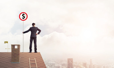 Businessman on house roof showing roadsign with money concept an