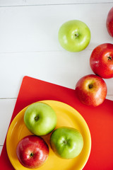 Top view of apples on a yellow plate and white wooden surface