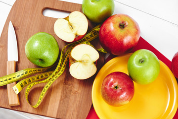 The concept of the diet. The view from the top of the apples lying in the dish, centimeter and a knife on wooden plate