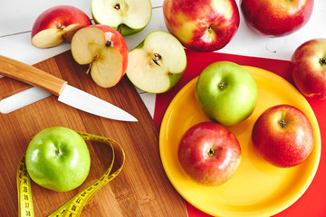 The view from the top of the apples lying in the dish, centimeter and a knife on wooden plate